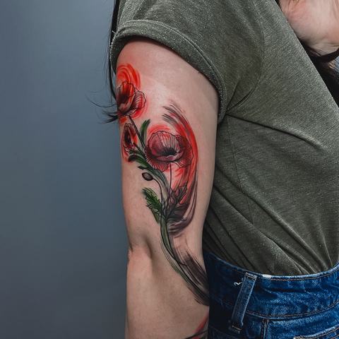 Bright red poppies bring colour to the forearm, while dark leaves and slender stems keep the floral arrangement elegant and visually balanced