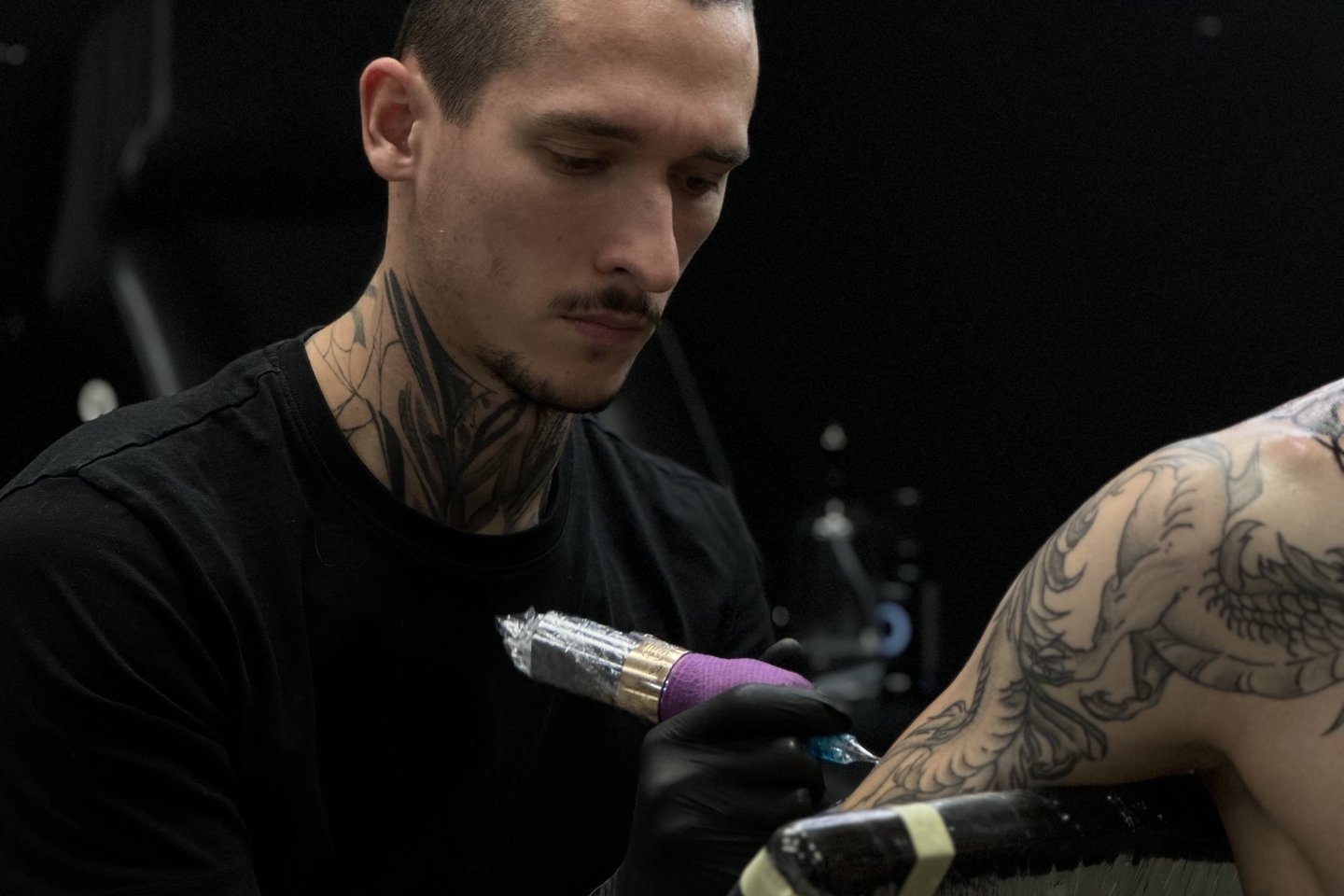 Tätoveerija mustades kinnastes töötab stuudios ringvalgusti all, tehes tätoveeringut modellile – praktilise hands-on õppe näide Tallinnas.
