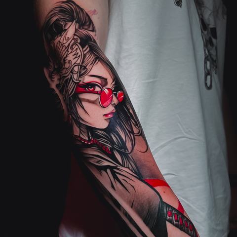A graphic female character is built from deep black areas and vivid red details, giving the forearm tattoo a bold and striking visual rhythm