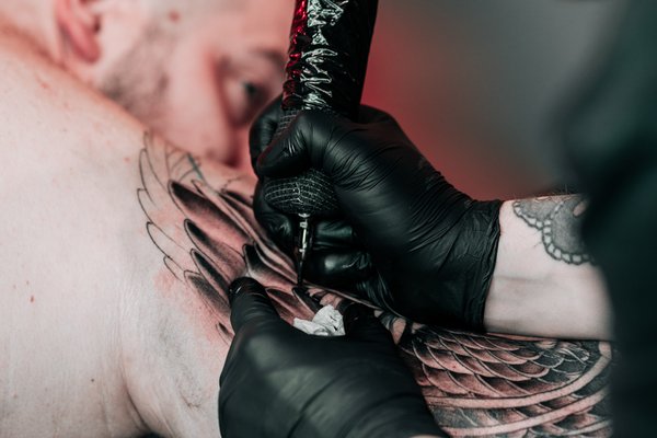 Kogenud tätoveerija VEAN TATTOO stuudios Tallinnas tätoveerib kliendi õlavarrele tiivamustriga disaini steriilses keskkonnas.