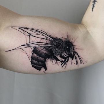 Black and grey bumblebee tattoo with finely detailed wings on the upper arm